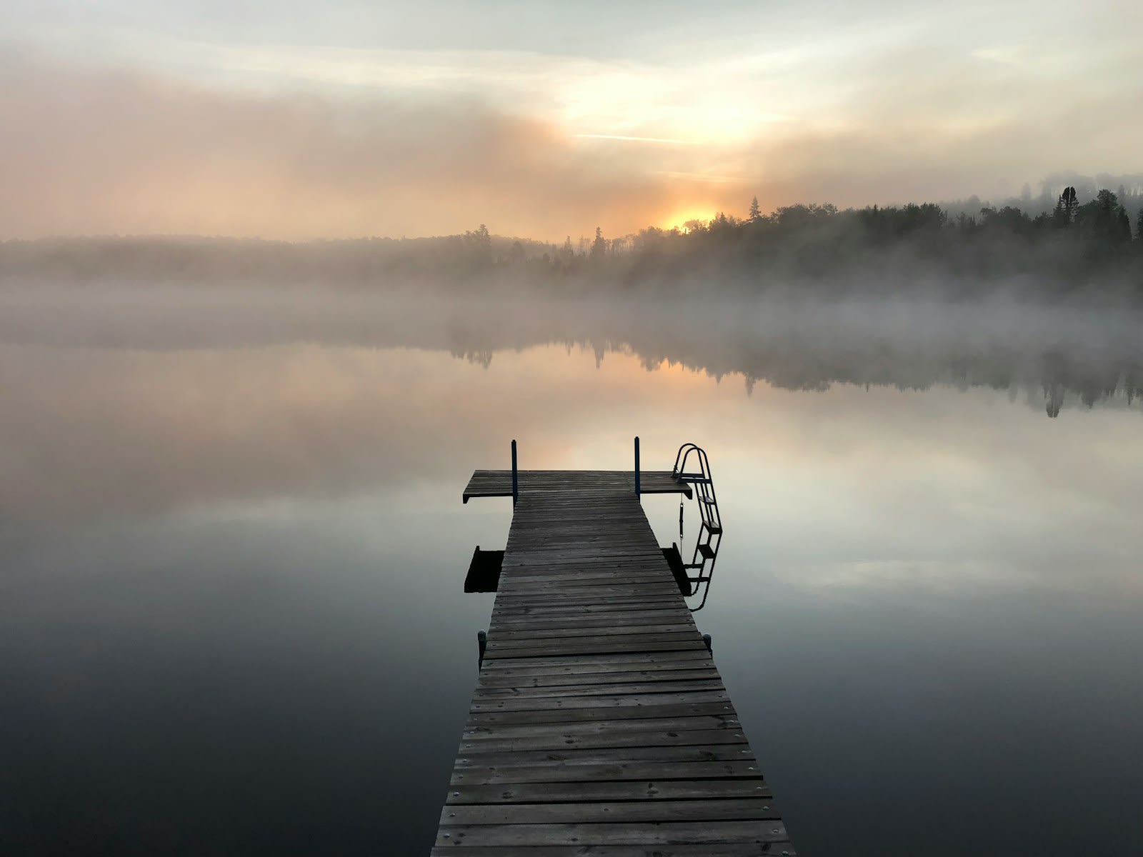 A wooden jetty on a still, misty lake at sunrise