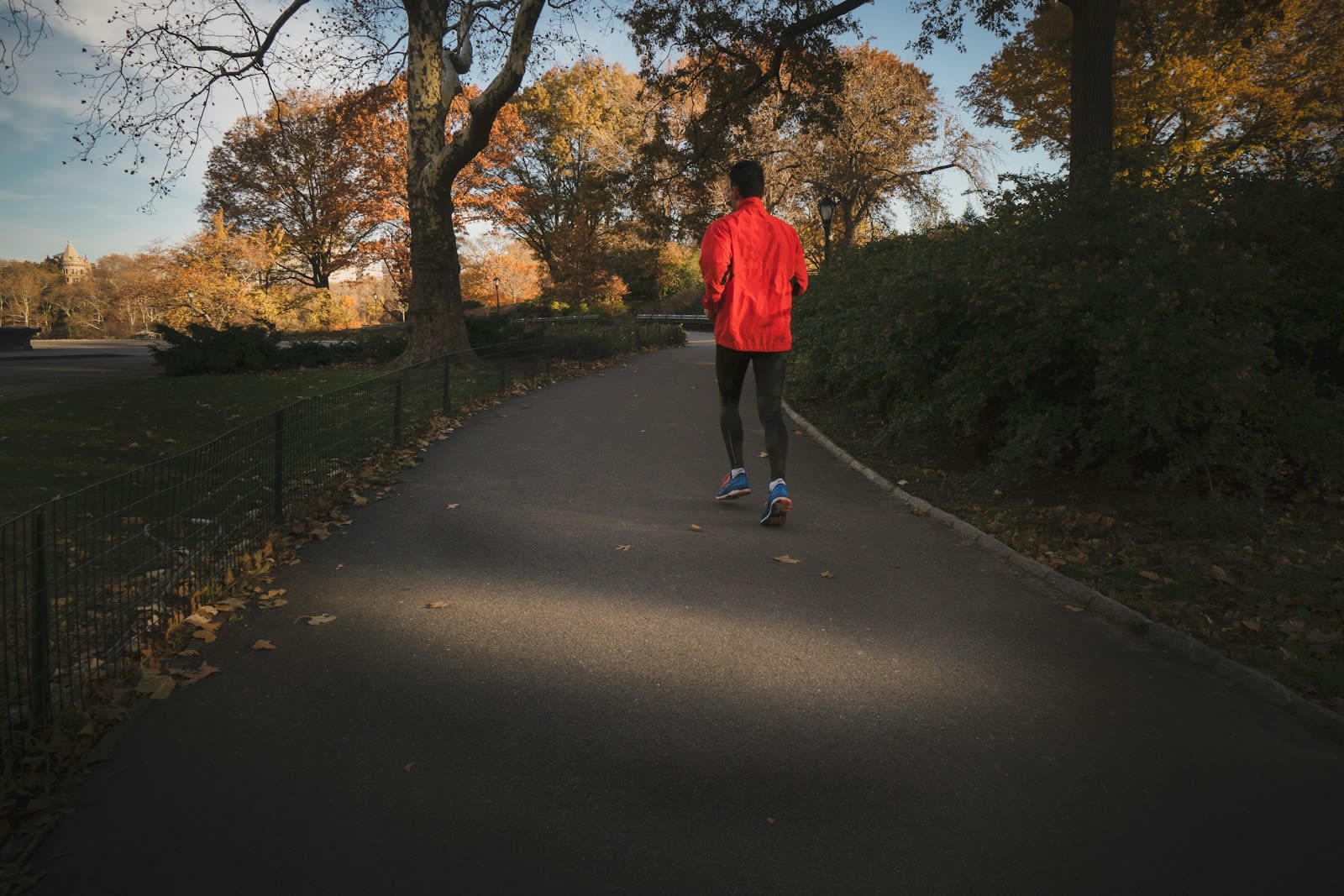 A man in a red jacket jogging along an autumn park path