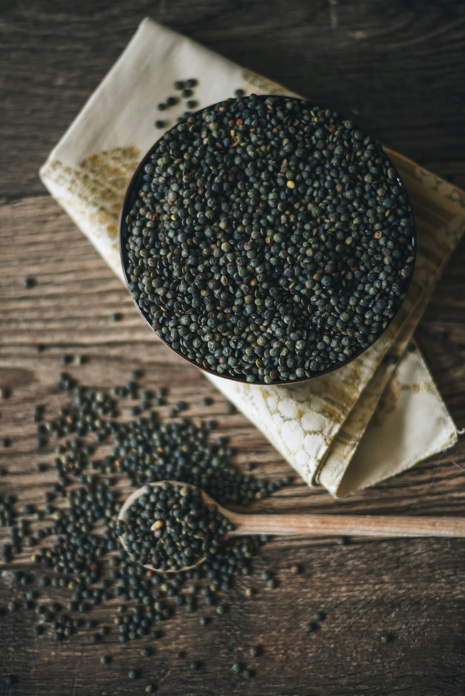 A bowl of dark green lentils on a wooden table