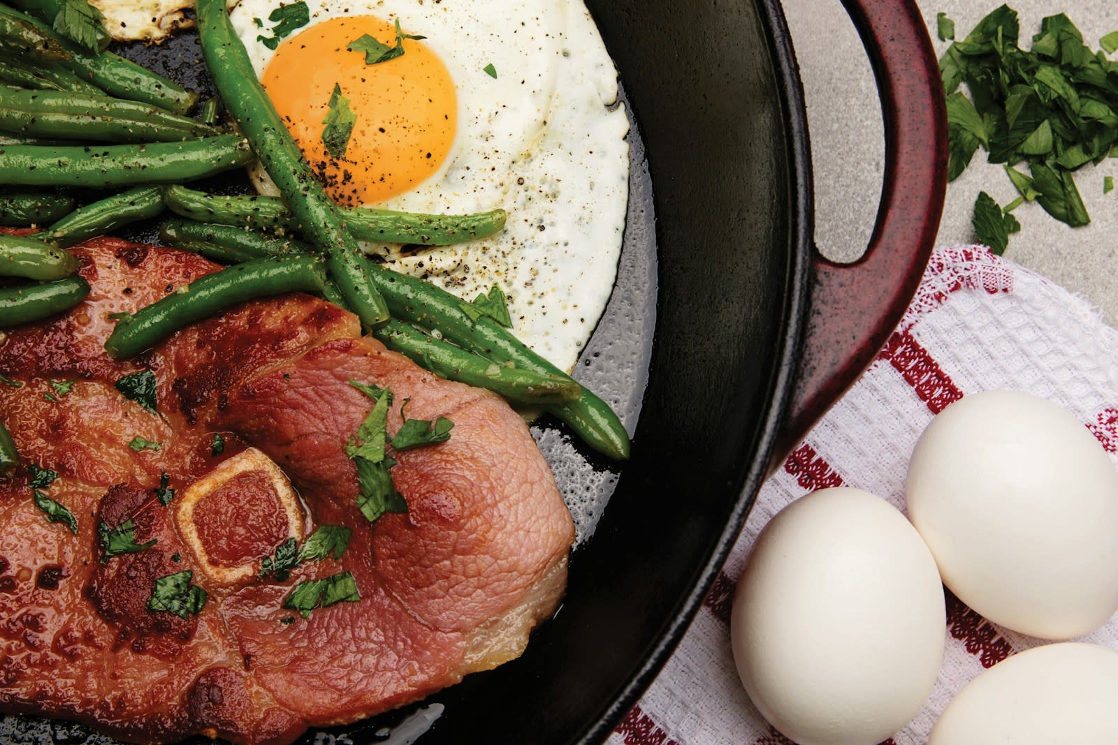 A plate of seared steak with green beans and a fried egg, with whole eggs on the side