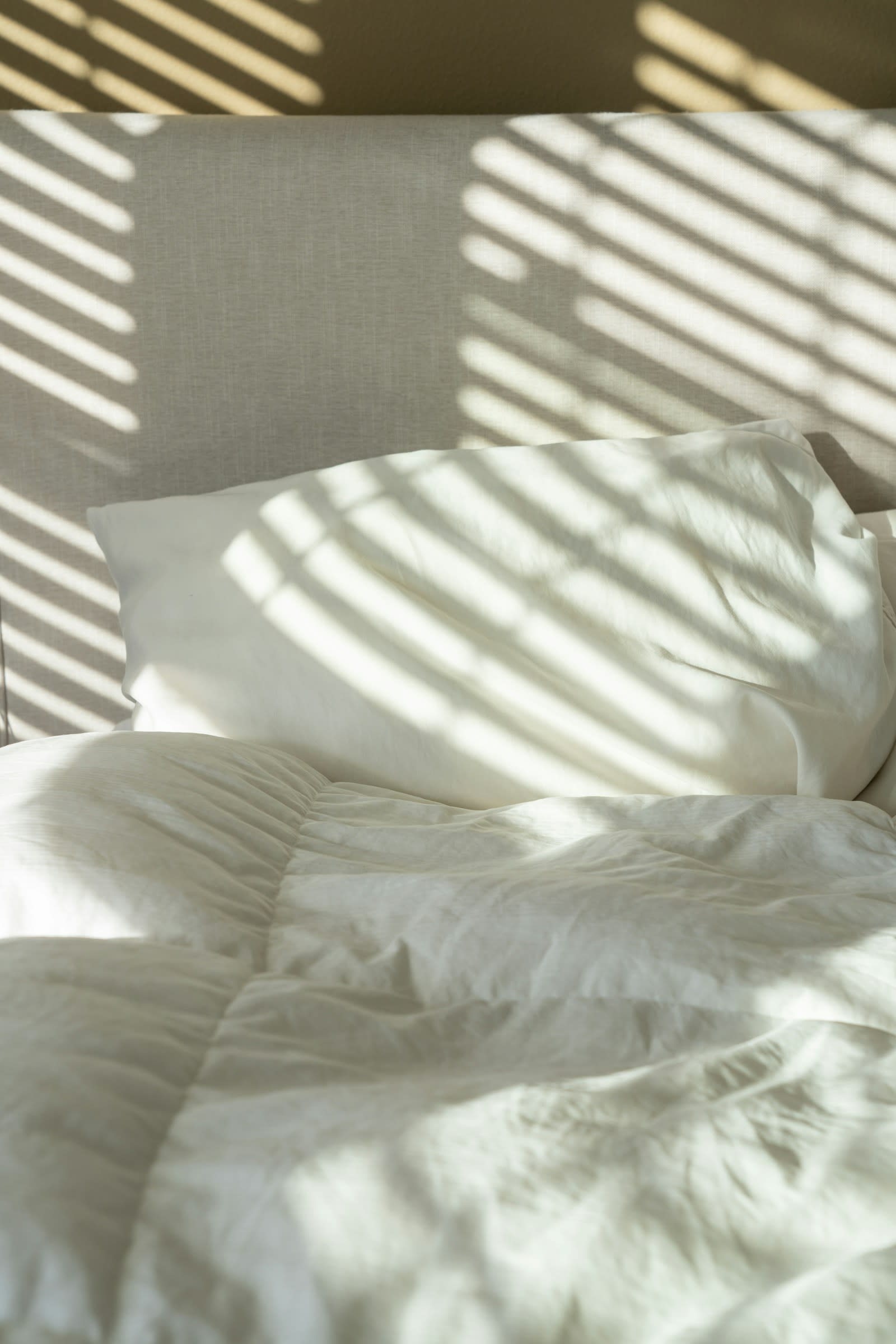 A bed with white sheets and pillows in soft morning sunlight