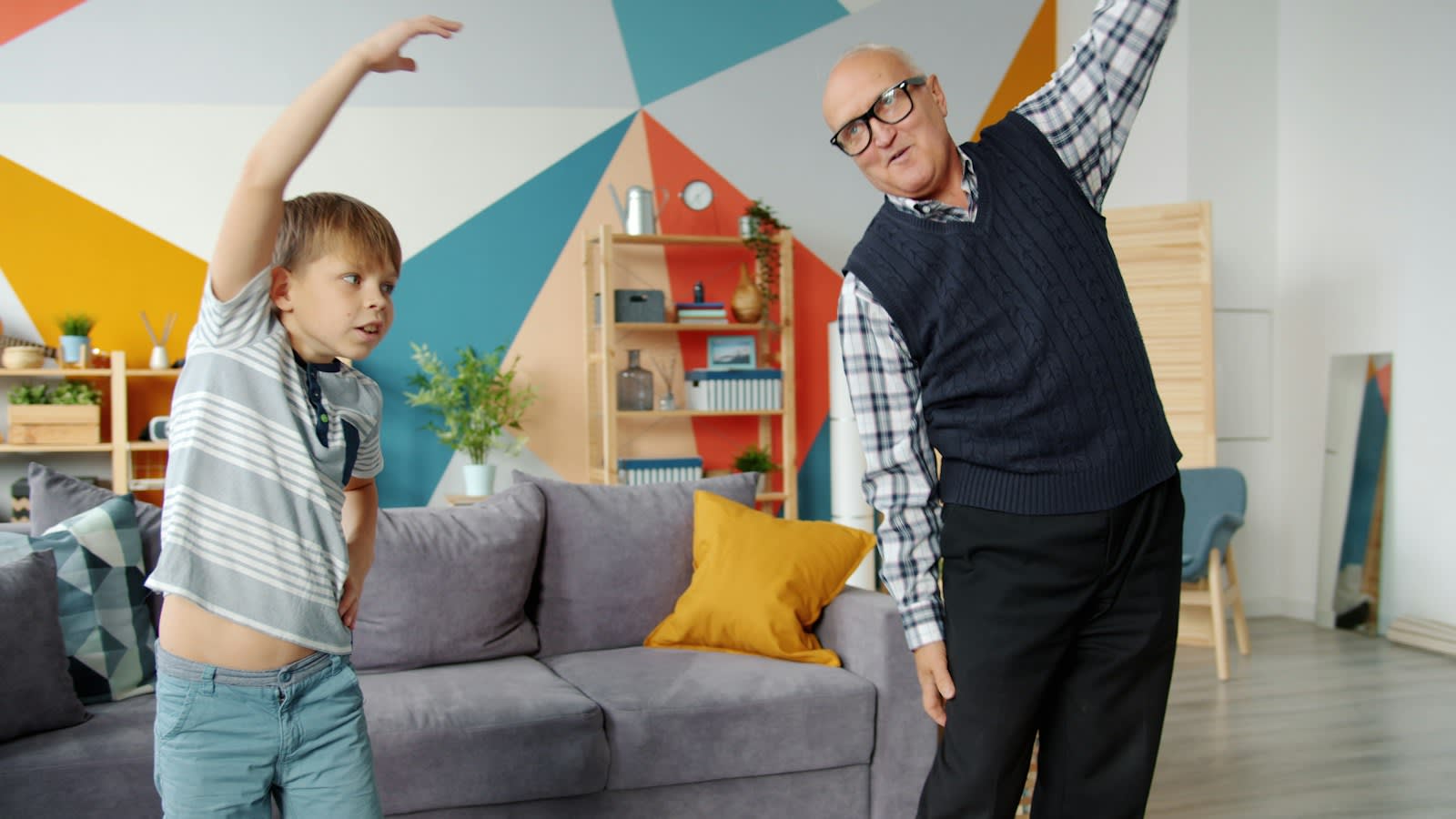 An older man and a boy doing a side stretch together at home