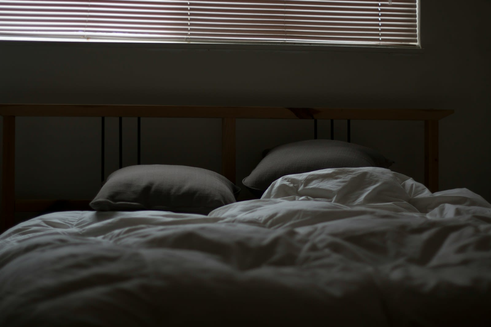 A dark, quiet bedroom with an unmade bed