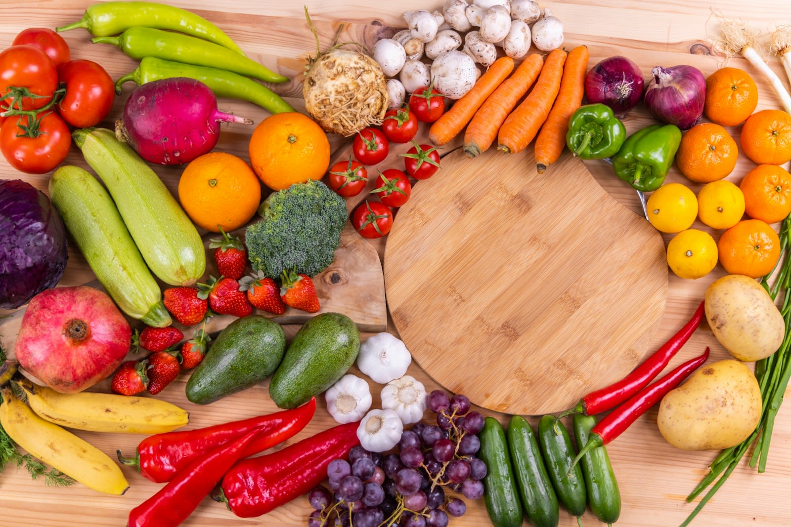 Fresh vegetables and fruit arranged around a wooden board