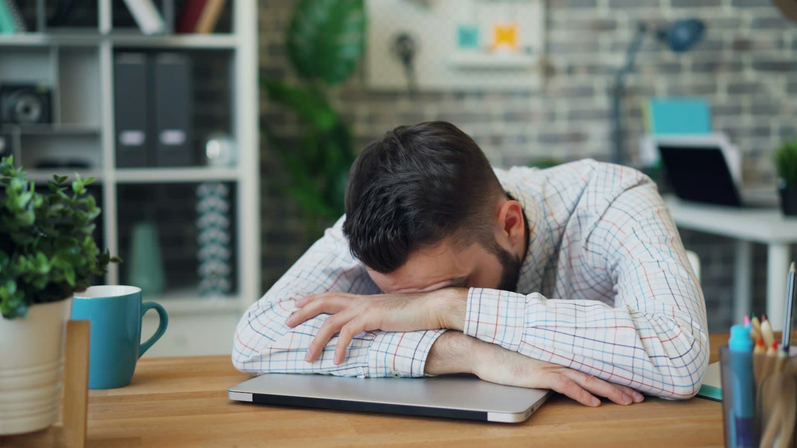 A tired man resting his head on his arms at a desk